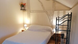 Une chambre à coucher avec un lit, une table de chevet, une lampe, une étagère avec des fleurs et un porte-revues en métal.