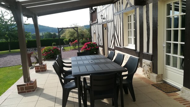 Une terrasse couverte avec une table et des chaises, une vue sur la campagne et un bâtiment à ossature en bois.