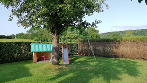 Un espace extérieur verdoyant avec une balançoire, un toboggan et un espace de repos abrité.