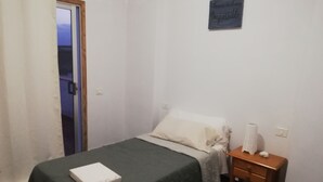 Un dormitorio pequeño y ordenado con una cama individual, una mesita de noche con lámpara y una puerta que da a otra habitación.