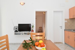 A dining area with a table, chairs, a TV, and a fruit bowl.