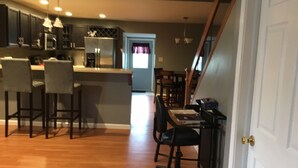 Une cuisine moderne avec des meubles de couleur sombre, un îlot central, des tabourets de bar et un coin repas comprenant une table et des chaises.