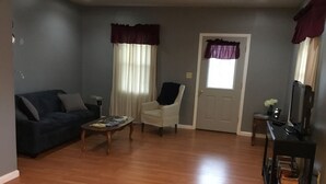 Un salon avec un canapé de couleur foncée, un fauteuil blanc, une table basse et un téléviseur posé sur un meuble.