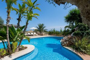 A clear blue pool surrounded by tropical plants and a stone wall.