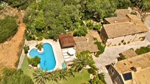 An aerial view of a property with a swimming pool, palm trees, and a stone building with a tiled roof.
