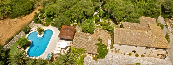 An aerial view of a property with a swimming pool, a covered patio, and a building with a tiled roof.
