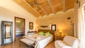 A bedroom with a bed, bedside table, lamp, and a view of the outside.