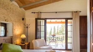A bedroom with a bed, a chair, a table with fruit, and a view of the outdoors.