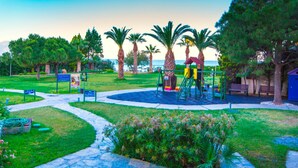 A playground with a slide and climbing structures, surrounded by trees and a pathway. - Hotel Ephesia (Kuşadası)