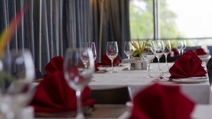 A dining table set with wine glasses and red napkins, with a view of the outdoors through large windows. - Crossroads Hotel Lae (Lae)