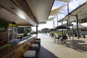 Un espace bar extérieur avec vue sur la piscine, des sièges et un comptoir en bois.