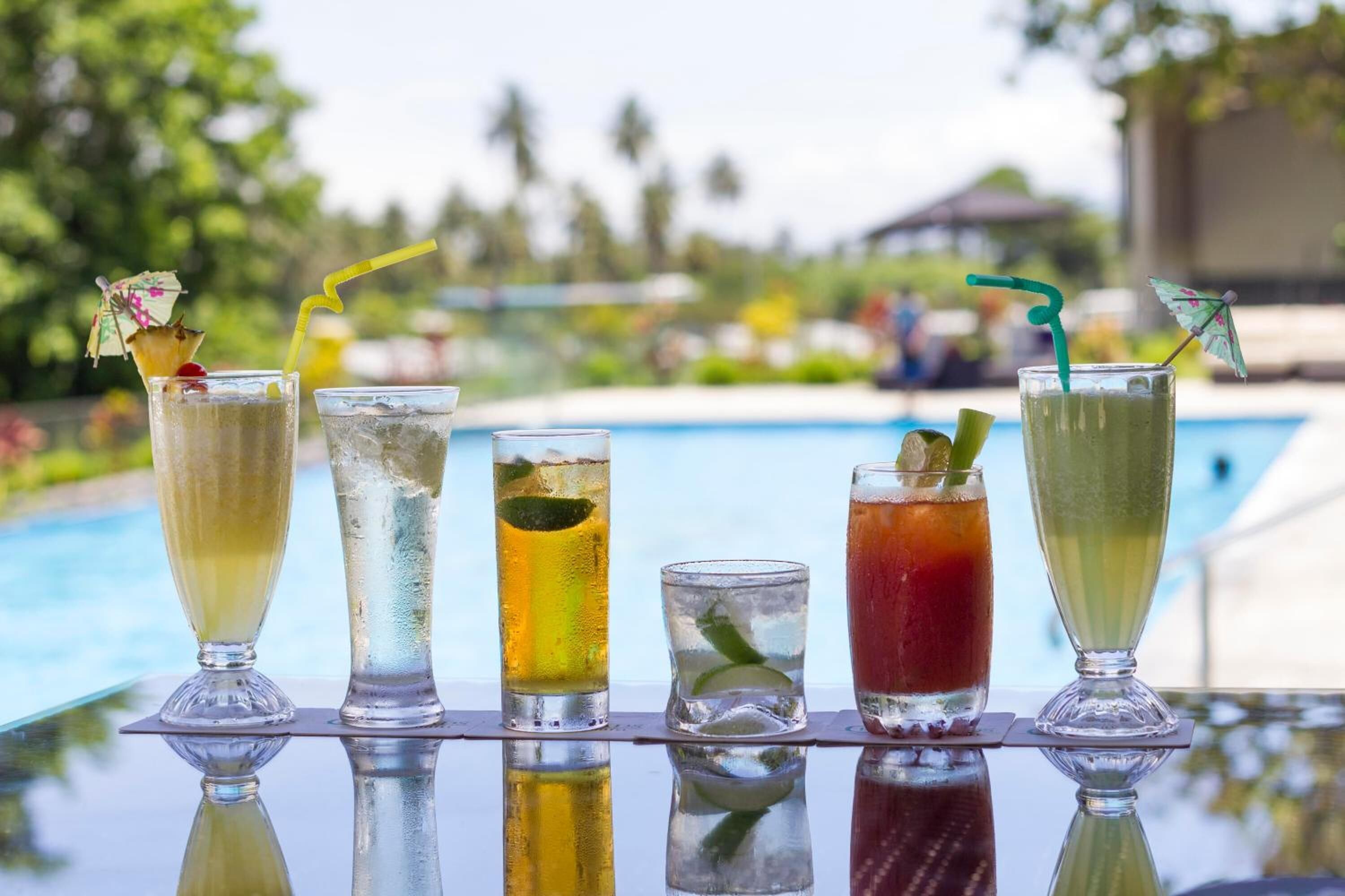 Une sélection de boissons est disposée sur une table près de la piscine, offrant une vue dégagée sur celle-ci et sur la végétation environnante.