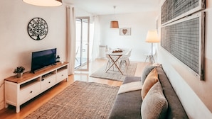 Een moderne woonkamer met een flatscreen televisie, een bank, een eettafel en een groot raam.