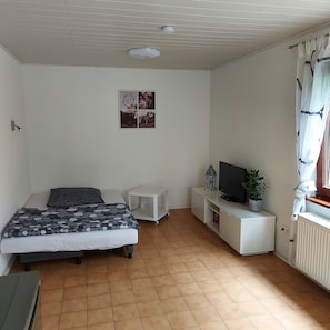 A bedroom with a bed, a TV, a small table, and a radiator.