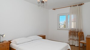 A bedroom with a bed, bedside tables, a desk, a chair, a window with curtains, and a chandelier. - ARBANIJA A1, budget 1-bedroom apartment, 80m from the beach (Arbanija)