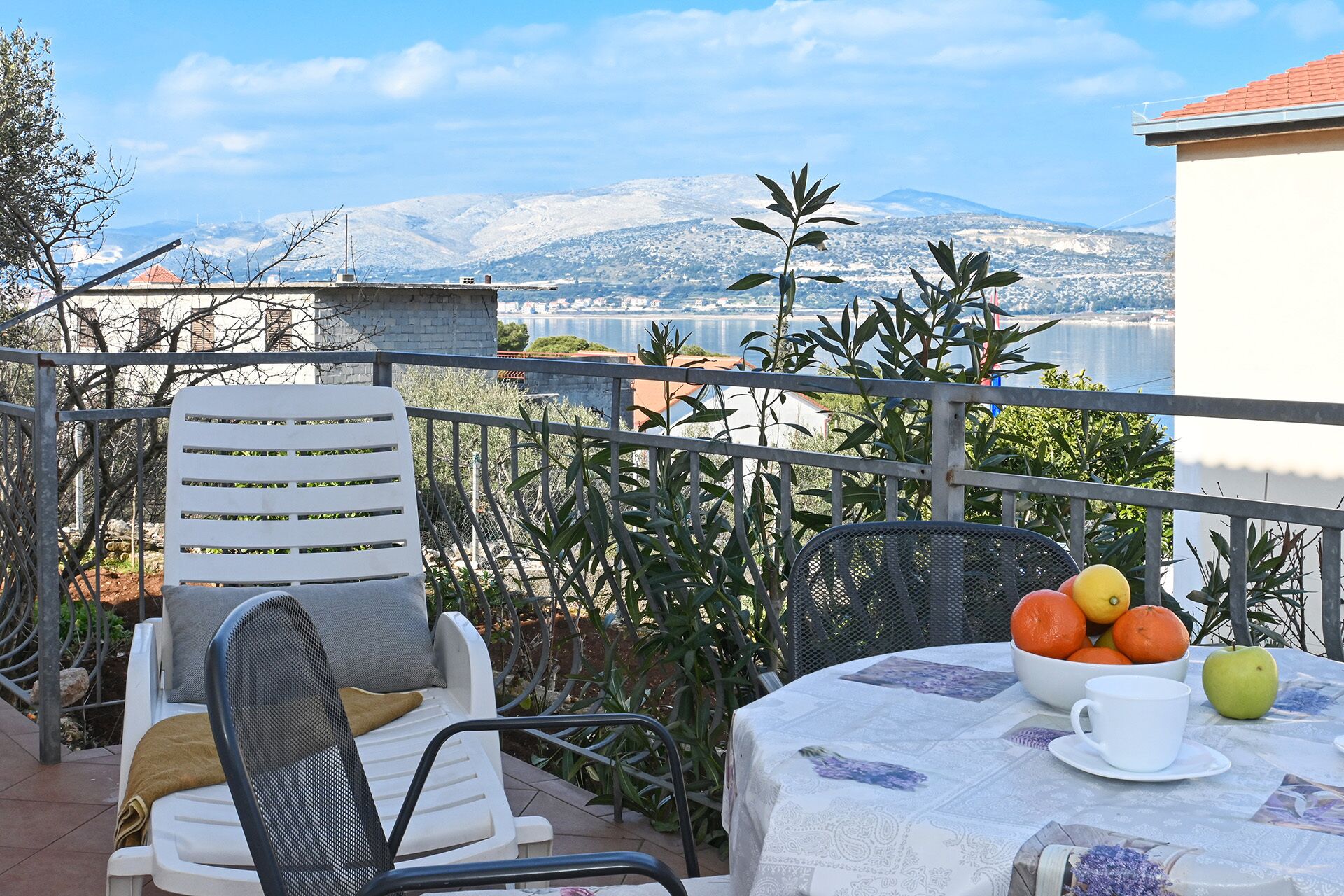 A balcony with a table set for two, featuring a bowl of fruit and a cup.