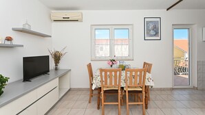 A dining area with a table set for four, a television on a counter, and a window with a view of buildings. - ARBANIJA A1, budget 1-bedroom apartment, 80m from the beach (Arbanija)