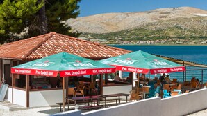 A seaside café with outdoor seating, red tiled roof, and umbrellas with 'PAN' branding. - ARBANIJA A1, budget 1-bedroom apartment, 80m from the beach (Arbanija)