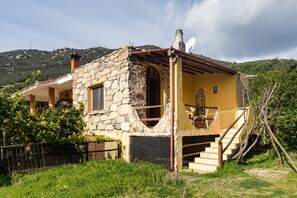 Une maison en pierre avec une façade jaune, une antenne parabolique et un escalier menant à l’entrée.