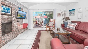 Un salon avec une cheminée en briques, un canapé en cuir rouge, une table basse en verre et un téléviseur fixé au mur.