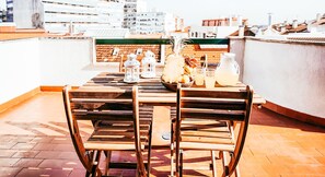 A wooden table with chairs on a rooftop terrace, equipped with lanterns, a fruit bowl, and a pitcher of lemonade.