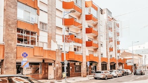 Un edificio de varios pisos con balcones naranjas y un estacionamiento al frente.