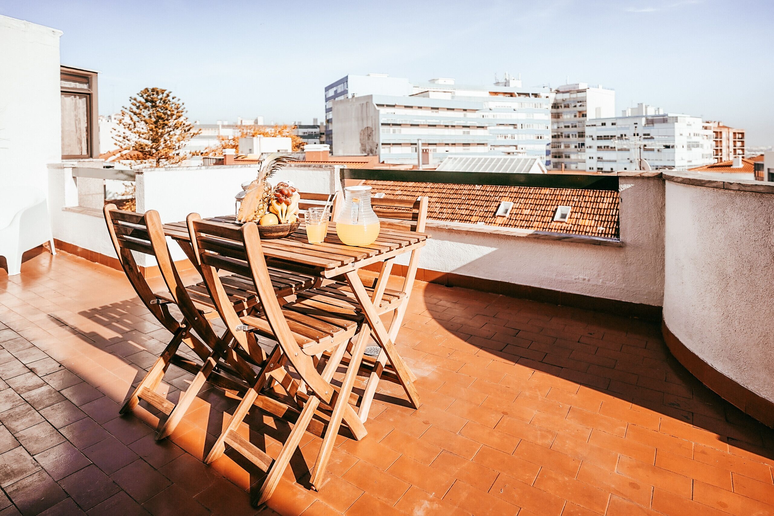 A wooden table and chairs on a rooftop terrace with a city view.