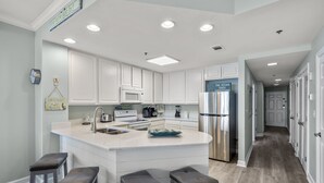 Une cuisine moderne avec des meubles blancs, un réfrigérateur en acier inoxydable et un îlot central doté de tabourets de bar.