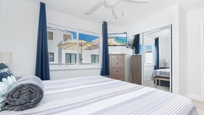 Ein Schlafzimmer mit einem Bett, einem Schminktisch, einem Kleiderschrank, einem Deckenventilator und einem Fernseher an der Wand.