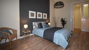 Un dormitorio con cama, mesitas de noche, una silla e imágenes colgadas en la pared.