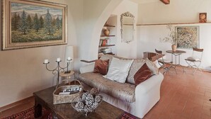 A cozy living room with a sofa, coffee table, and decorative items. There is a painting on the wall, a mirror, and a small table with chairs. - UNDER THE TUSCAN SUN (scandicci)