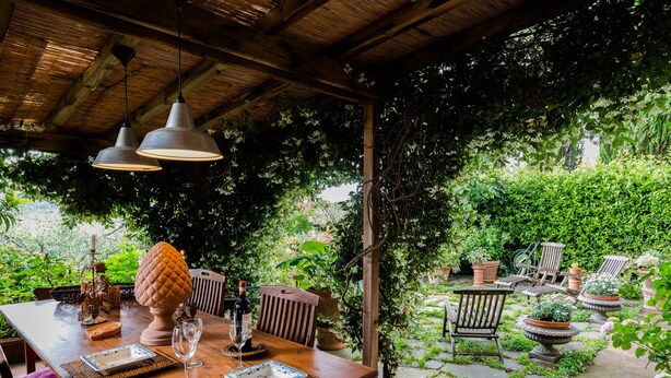 An outdoor dining area with a wooden table set for two, surrounded by lush greenery and potted plants. - UNDER THE TUSCAN SUN (scandicci)