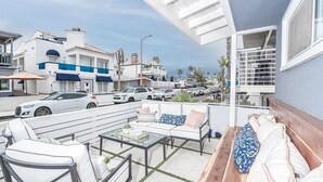 A balcony with outdoor seating, a view of parked cars, and buildings in the background.