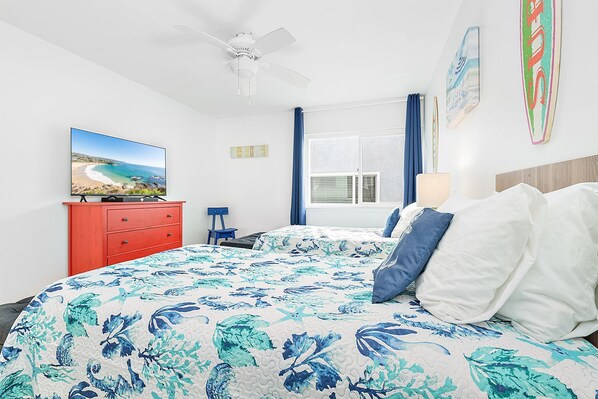 A bedroom with a bed, a TV, a dresser, a ceiling fan, and a window with curtains.