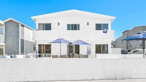 A two-story building with a flat roof, a balcony on the left, and a patio area with umbrellas.