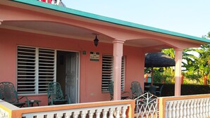 A pink building with a covered porch, outdoor seating, and a sign indicating a house number. - Casa Leyani y Osvedy (Viñales)