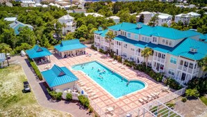 Ett flygbildsfoto av ett semesterområde med en stor swimmingpool, omgiven av avslappningsområden och en överbyggd paviljong.