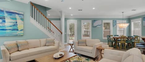 A spacious living room with a high ceiling, a ceiling fan, and a dining area with a chandelier.