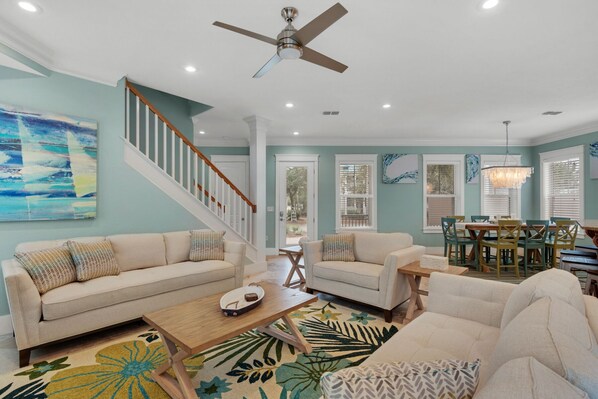 A spacious living room with a high ceiling, a ceiling fan, and a dining area with a chandelier.