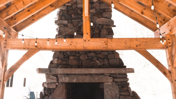 Une cheminée en pierre sous un toit en bois, illuminée de guirlandes lumineuses.