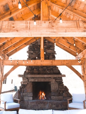 A stone fireplace under a wooden roof with string lights. - The Dogtrot in Dennis Cove - Creekside Cabin w/ Sauna, Hot Tub & AT Trail Access (Hampton)