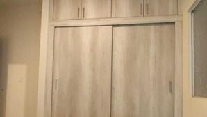 Une pièce avec une grande armoire, un lit recouvert d’une courtepointe bleue et une fenêtre sur le côté droit.