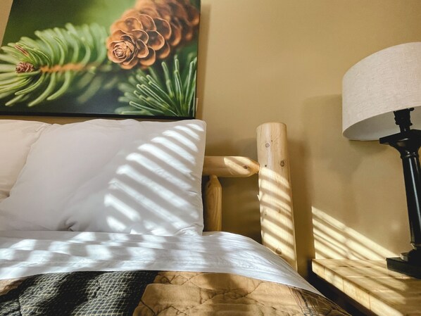 A bed with white bedding, a wooden headboard, a lamp, and a painting of pine cones and needles on the wall. - Cedar Spring Lodge, near JFBB Ski, Private Fire Pit, Hot Tub, WiFi, & Game Room (Lake Harmony)
