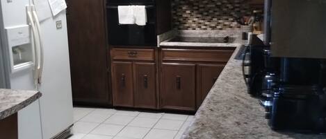 A kitchen with dark wooden cabinets, a white refrigerator, a tiled backsplash, and a granite countertop.