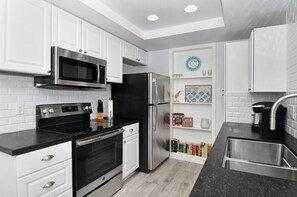 Enjoy cooking in this well-equipped kitchen with stainless steel appliances, white cabinetry, and a black countertop.
