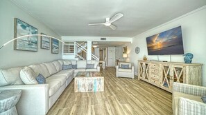 A spacious living room with a sectional sofa, a coffee table, and a wooden floor. There is a staircase leading to another level, and a large painting on the wall. - LaPlaya 205D! Spectacular views! (Longboat Key)