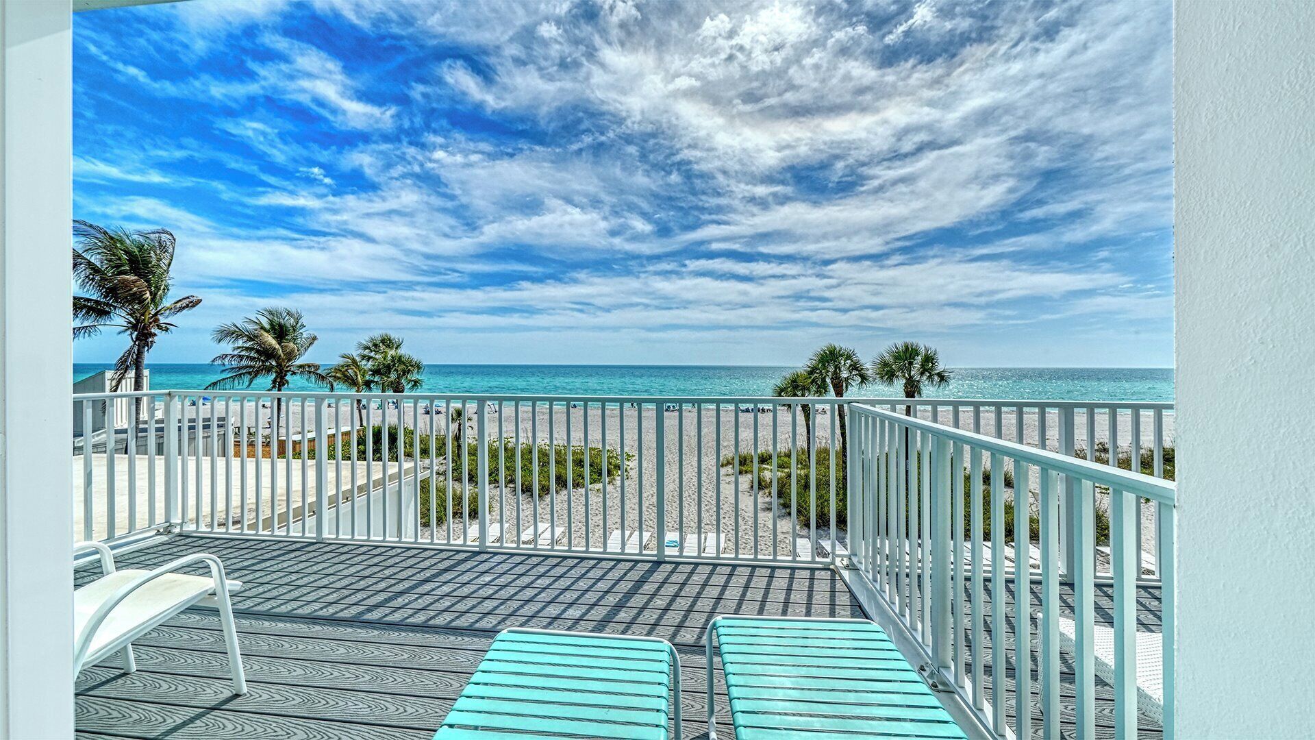 A balcony with a view of the beach and ocean, metal railings, and a patterned floor.