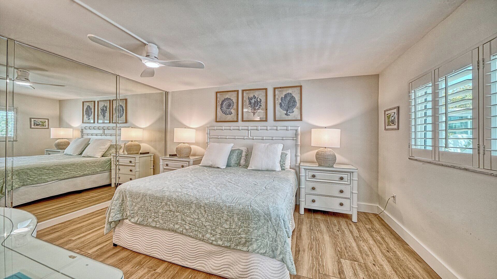 A bedroom with a bed, bedside tables, lamps, a ceiling fan, and framed artwork on the wall.
