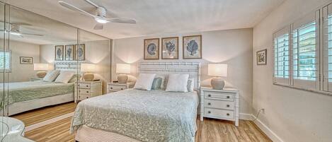 A bedroom with a bed, bedside tables, lamps, a ceiling fan, and framed artwork on the wall.