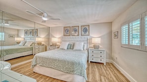 Une chambre à coucher comprenant un lit, des tables de chevet, des lampes, un ventilateur de plafond et des œuvres d’art encadrées accrochées au mur.
